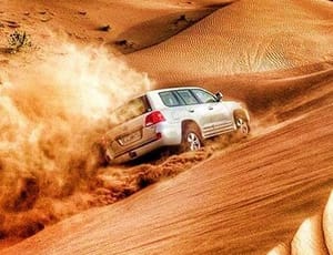 Sensational Ras Al Khaimah Getaway with Desert Safari White SUV driving down a steep sand dune in the desert, creating a large dust cloud during an off-road safari adventure